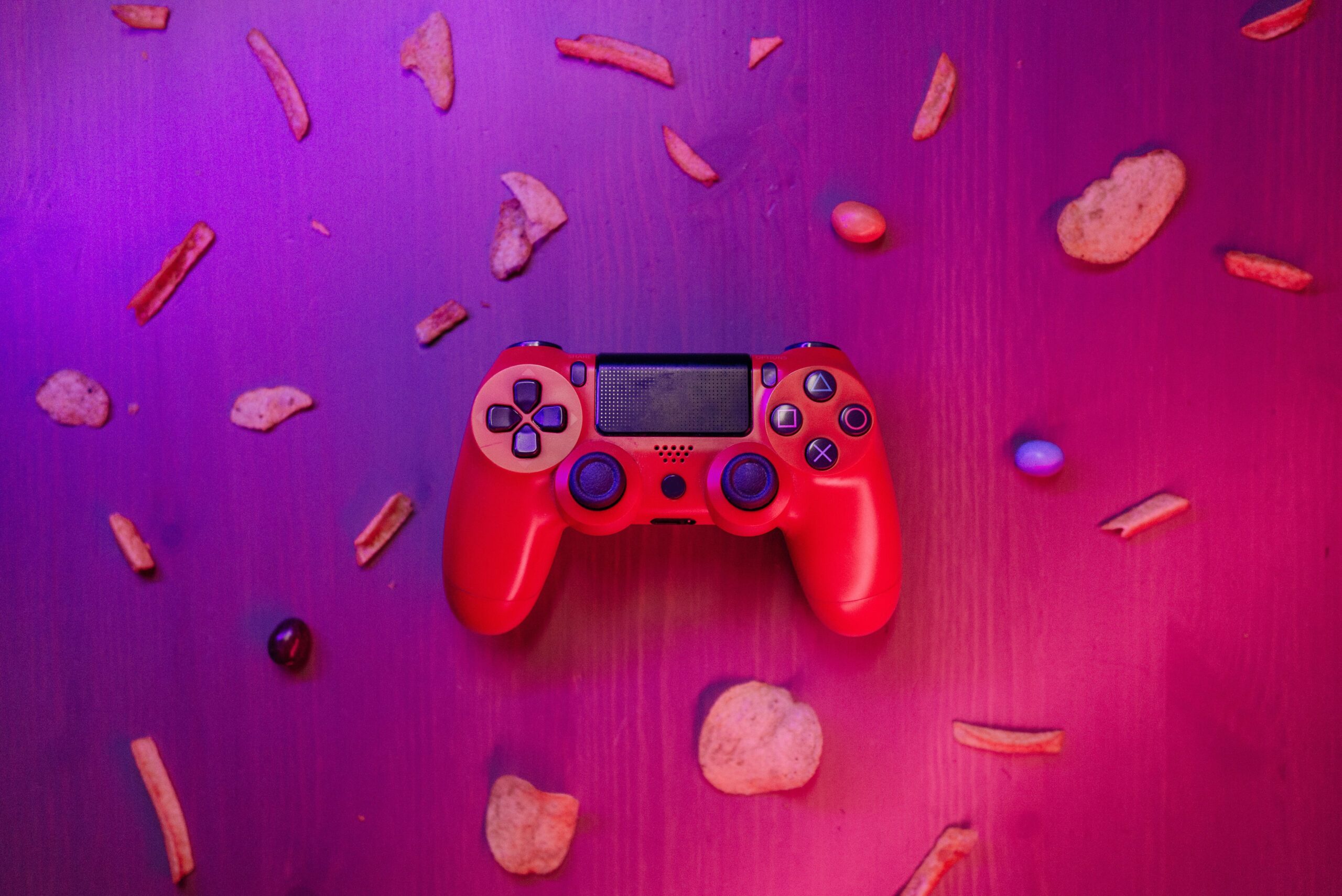 Stylish red game controller surrounded by snacks on a vibrant purple background.